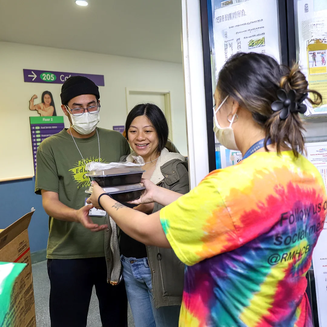 RMHC Bay Area staff member hands packaged meals to two smiling individuals at a hospital through the Feed the Love program.