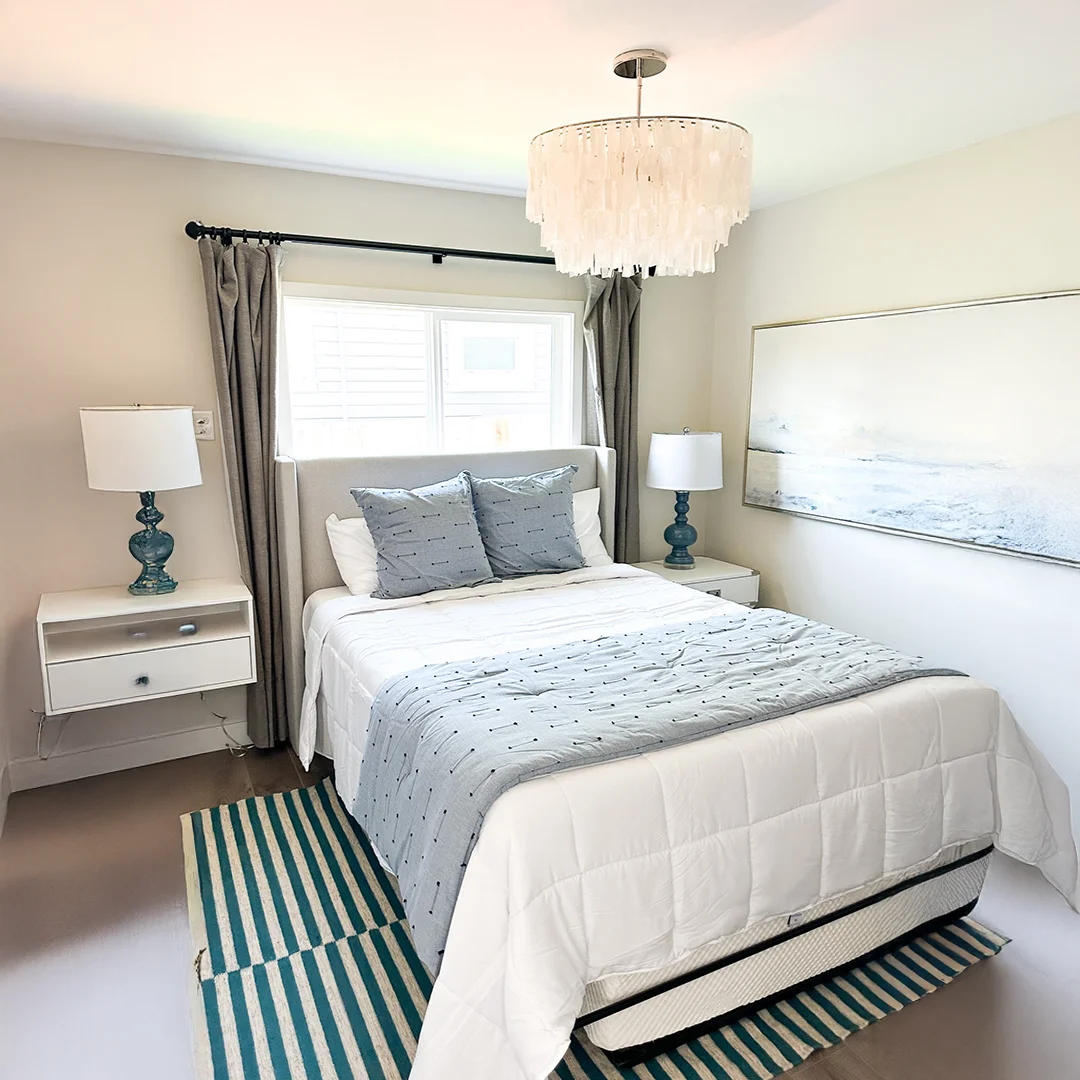 Bright guest bedroom with a modern chandelier, cozy white bedding, and soft gray and blue decor at RMHC Oakland.